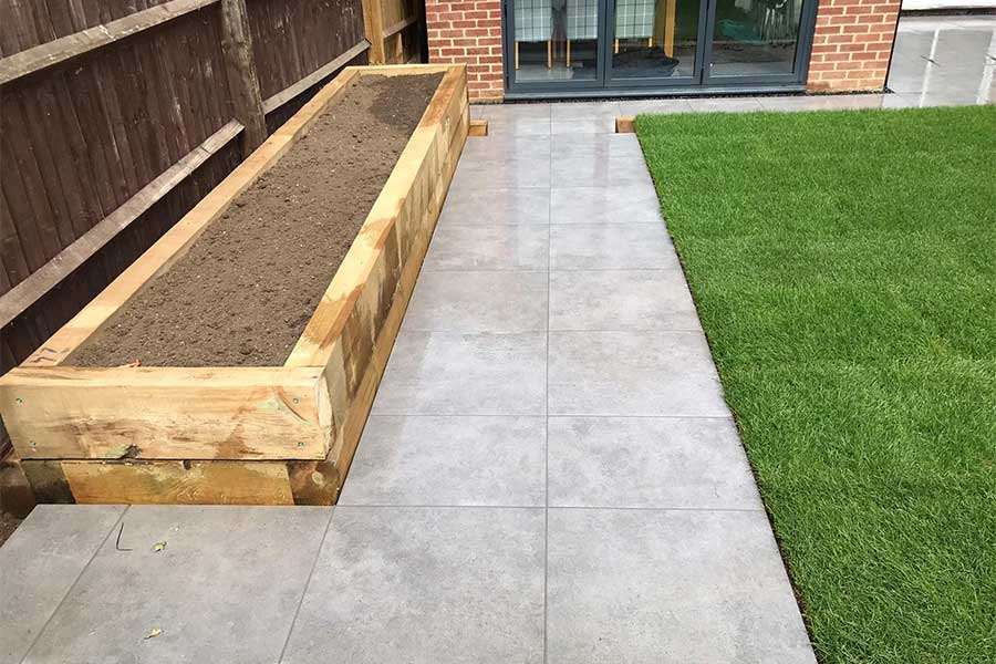 A smart and modern porcelain paved garden path running alongside raise timber sleeper beds