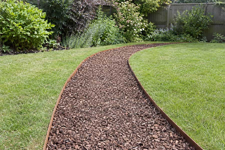 A simple woodchip garden path with metal edging leading across a lawn